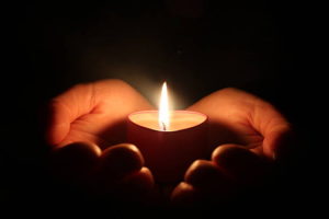 hands holding one candle in darkness